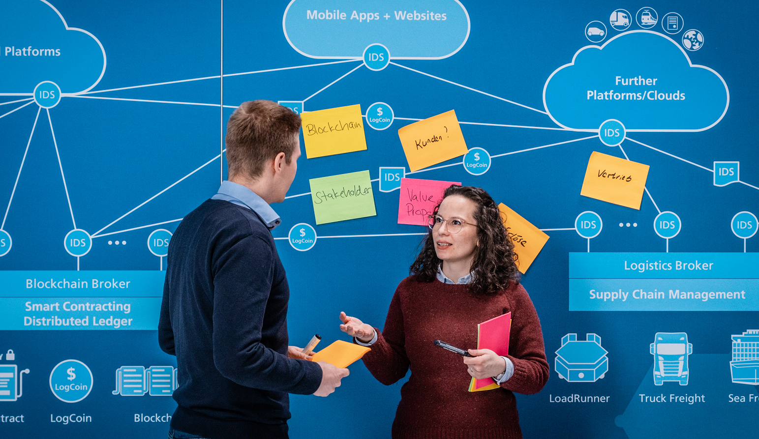 Das Bild zeigt zwei Personen im Gespräch über Blockchain-Geschäftsmodelle. Ihre gestenreiche Diskussion verdeutlicht die Bedeutung von Innovationsmanagement und Transformationsmanagement für die digitale Wirtschaft. Dezente Symbole im Hintergrund unterstreichen die Vernetzung und Dezentralisierung der Blockchain-Technologie.