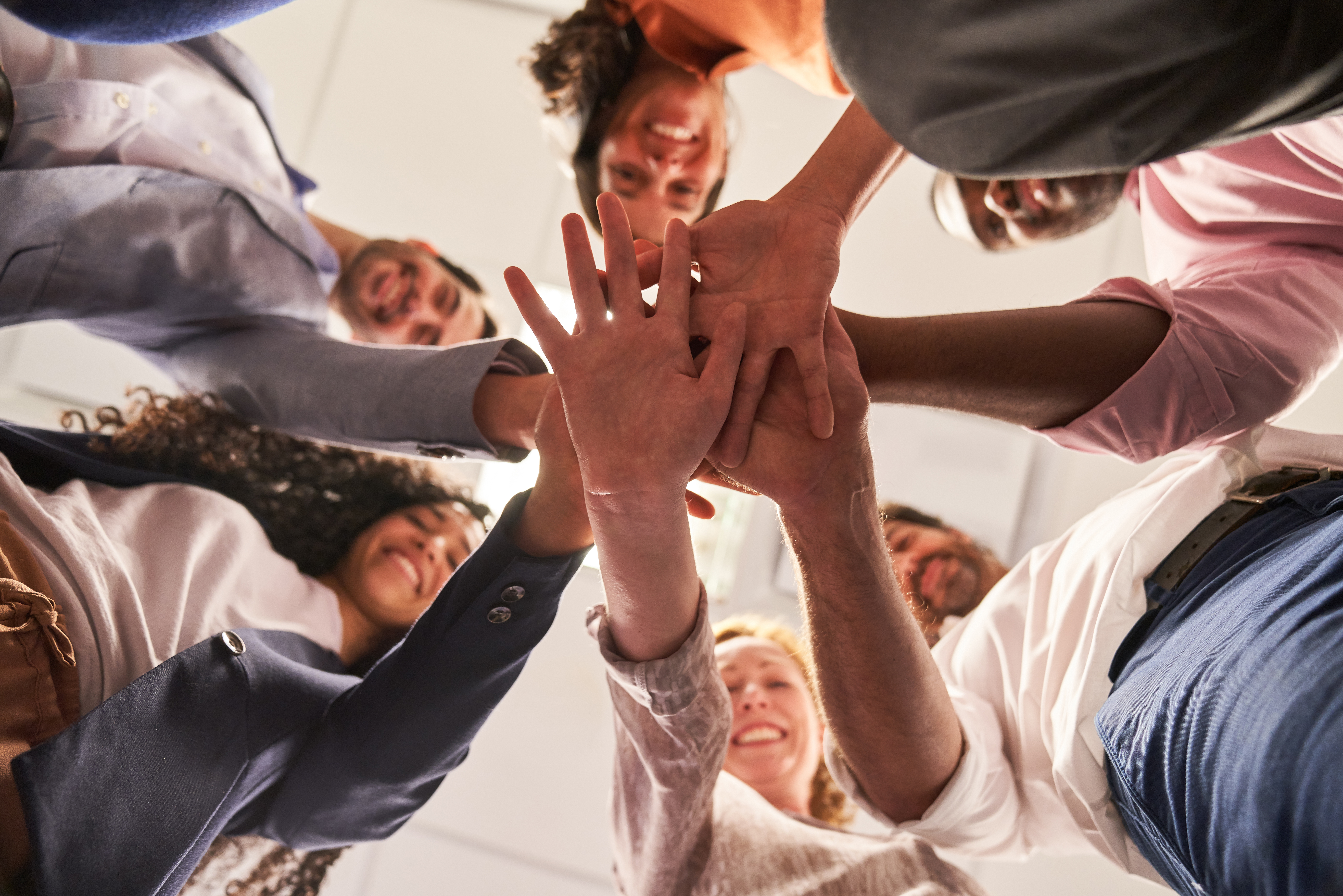 Das Bild zeigt eine Gruppe von Menschen, die ihre Hände übereinander legen, symbolisch für Kollaboration statt Konkurrenz. Diese Geste verdeutlicht das Prinzip der Zusammenarbeit, das in Open-Source-Strategien eine zentrale Rolle spielt. Die Gruppe steht für den gemeinsamen Austausch von Ideen und Ressourcen, um durch offene und kooperative Ansätze innovative Lösungen zu entwickeln.