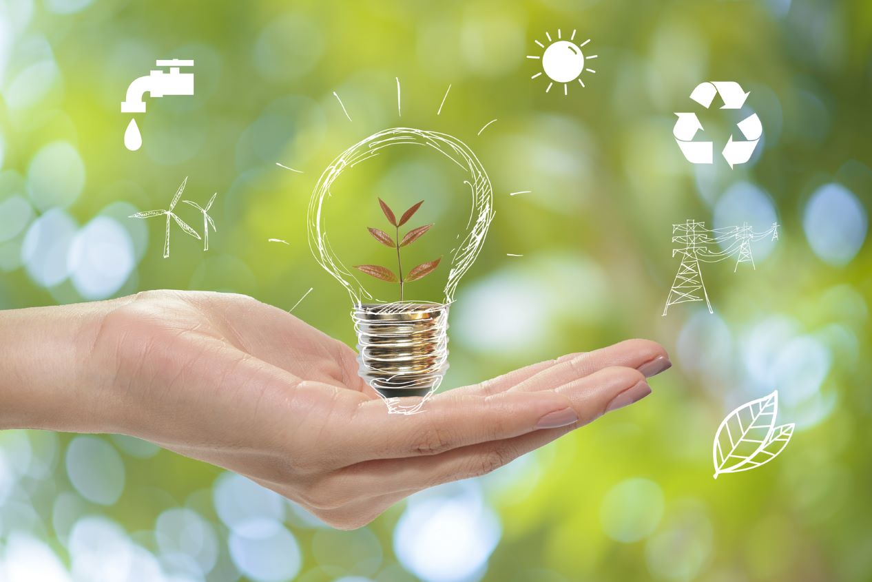 Das Bild zeigt eine Hand, die eine gezeichnete Glühbirne mit einer innenwachsenden Pflanze hält, umgeben von Symbolen für Wasser, Sonne, Recycling, Windkraft und Energie. Es symbolisiert Nachhaltigkeit in der Logistik und steht u.a. für das Leistungsangebot des Fraunhofer IML.