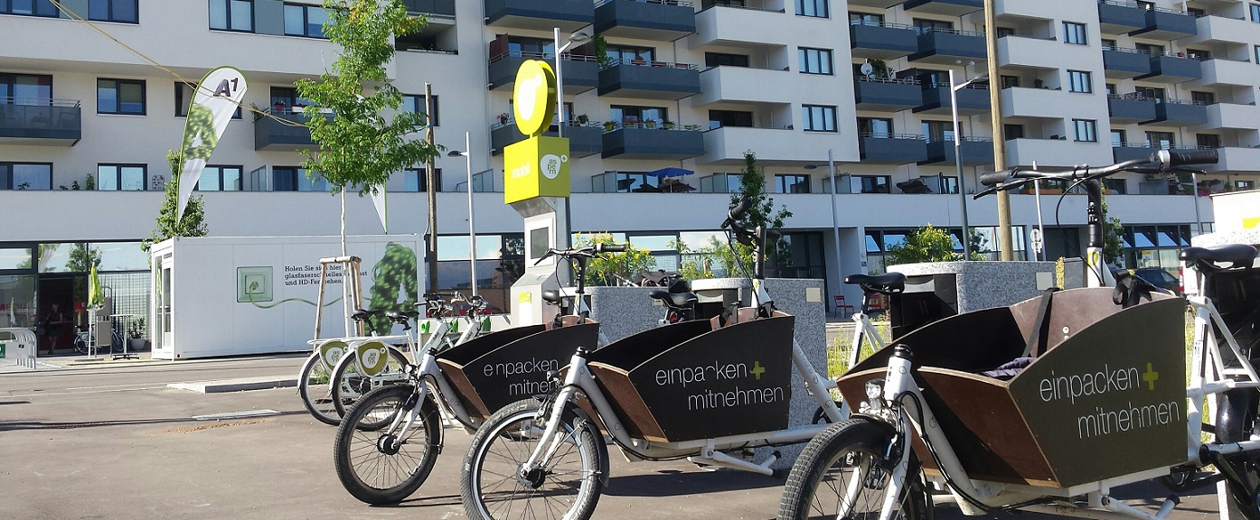 Das Bild zeigt eine Lastenradflotte zum Verleih vor Wohnhäusern. Es symbolisiert die Möglichkeiten der nachhaltigen Mobilität für Städte.