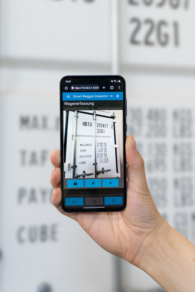 SWIn Software am Smartphone Hand die ein Smartphone vor einen Container hält, um mit der SWIn Software einen Wagen zu erfassen.