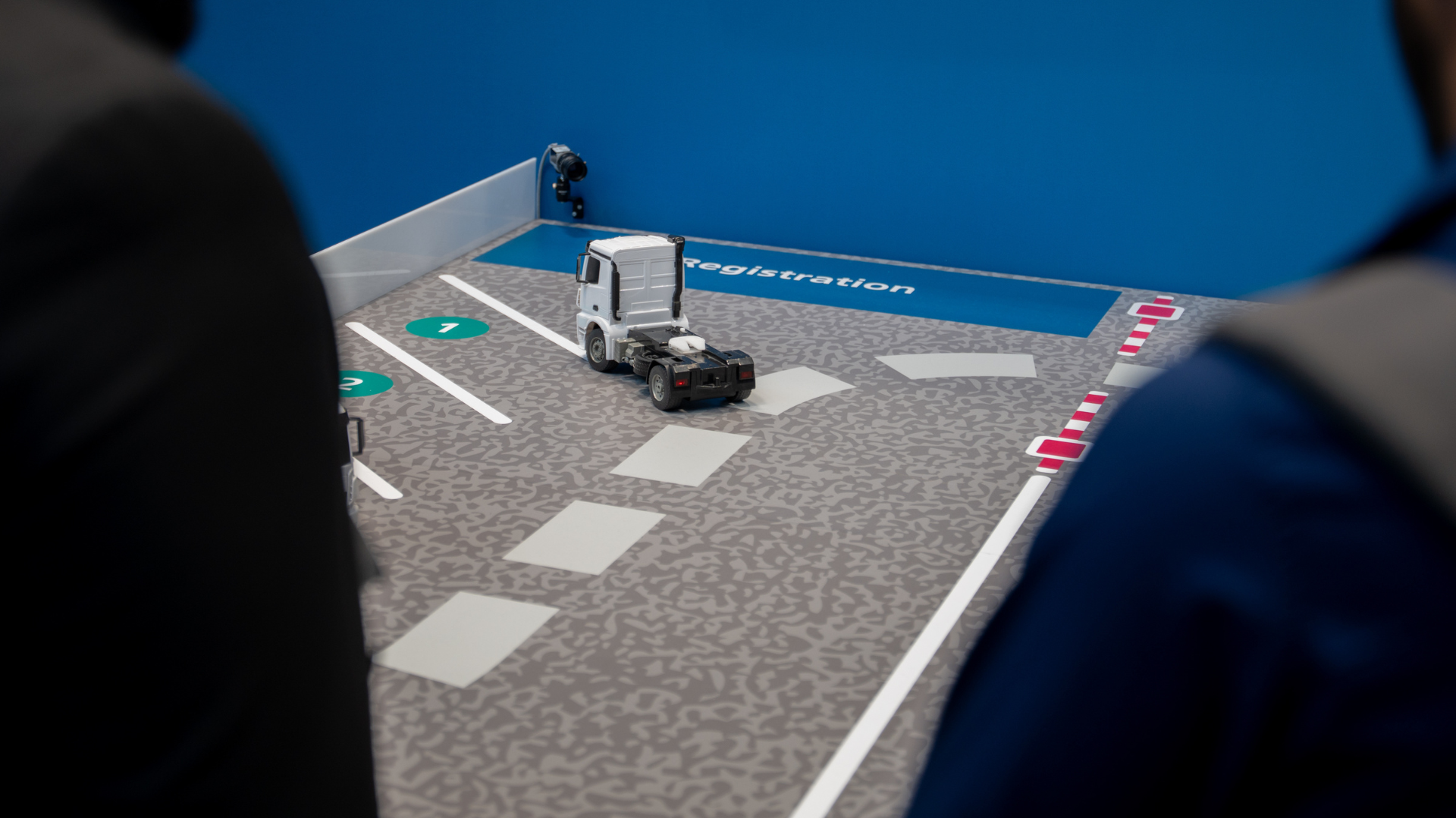 Model of an automated vehicle in a parking lot with people in the foreground observing the scenario