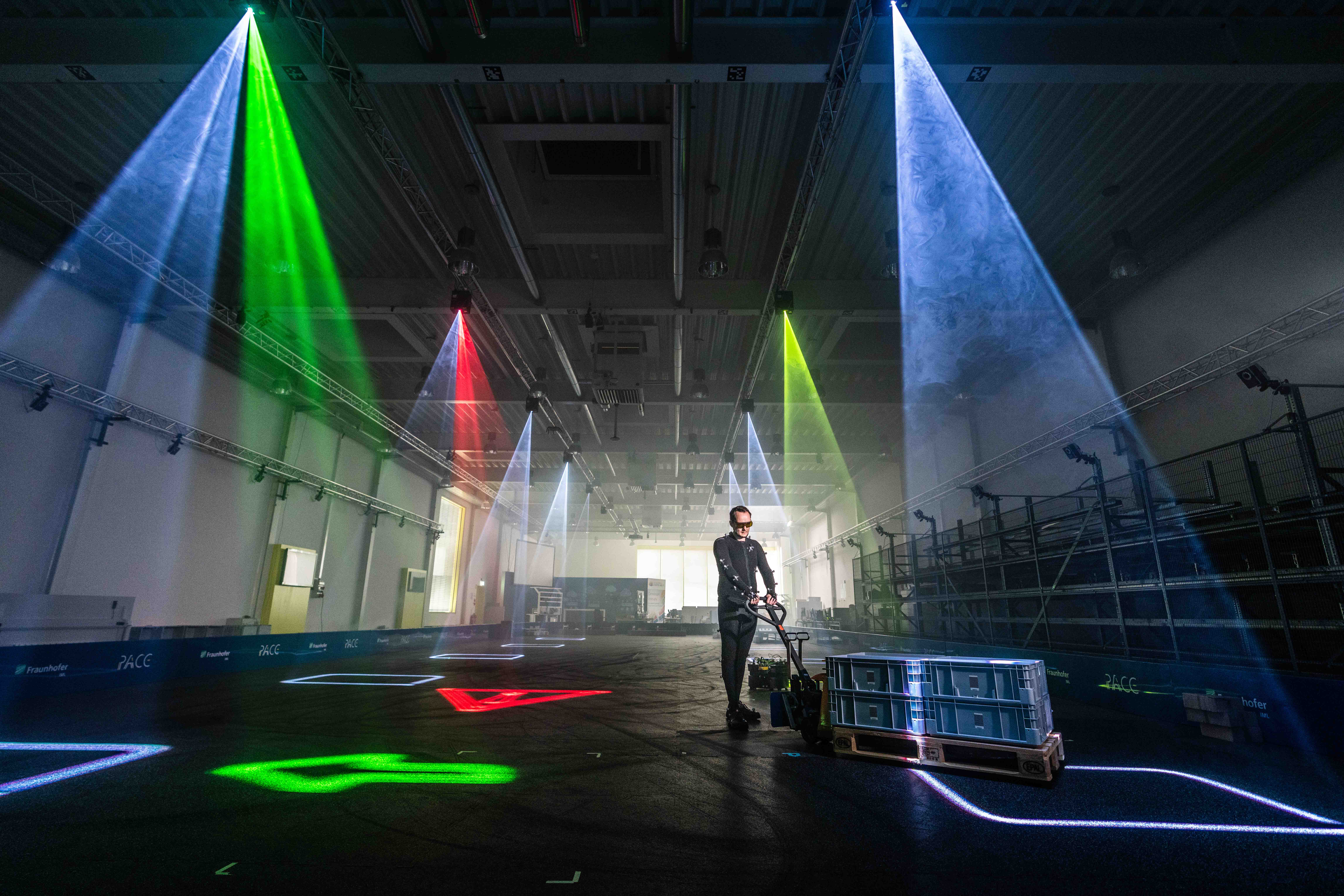 Symbolisch für das Pace Lab und für die Bedeutung der Nachhaltigkeit in der Logistik - Ein Mitarbeiter im Logistikbereich arbeitet in einer modernen Lagerhalle, beleuchtet von farbigen Lichtstrahlen.