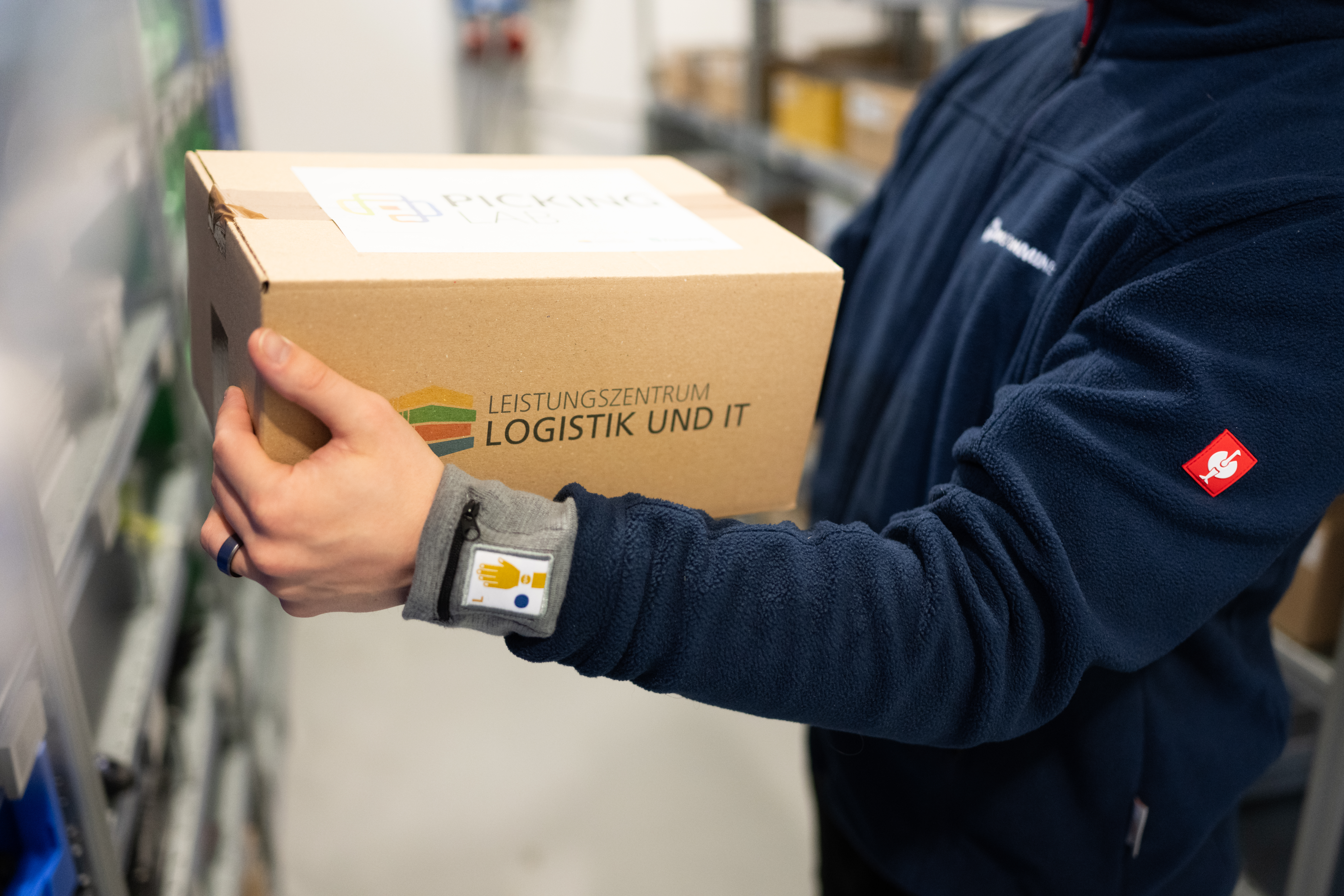 Mitarbeiter trägt eine Box mit Hilfe des Picking Labs Systems