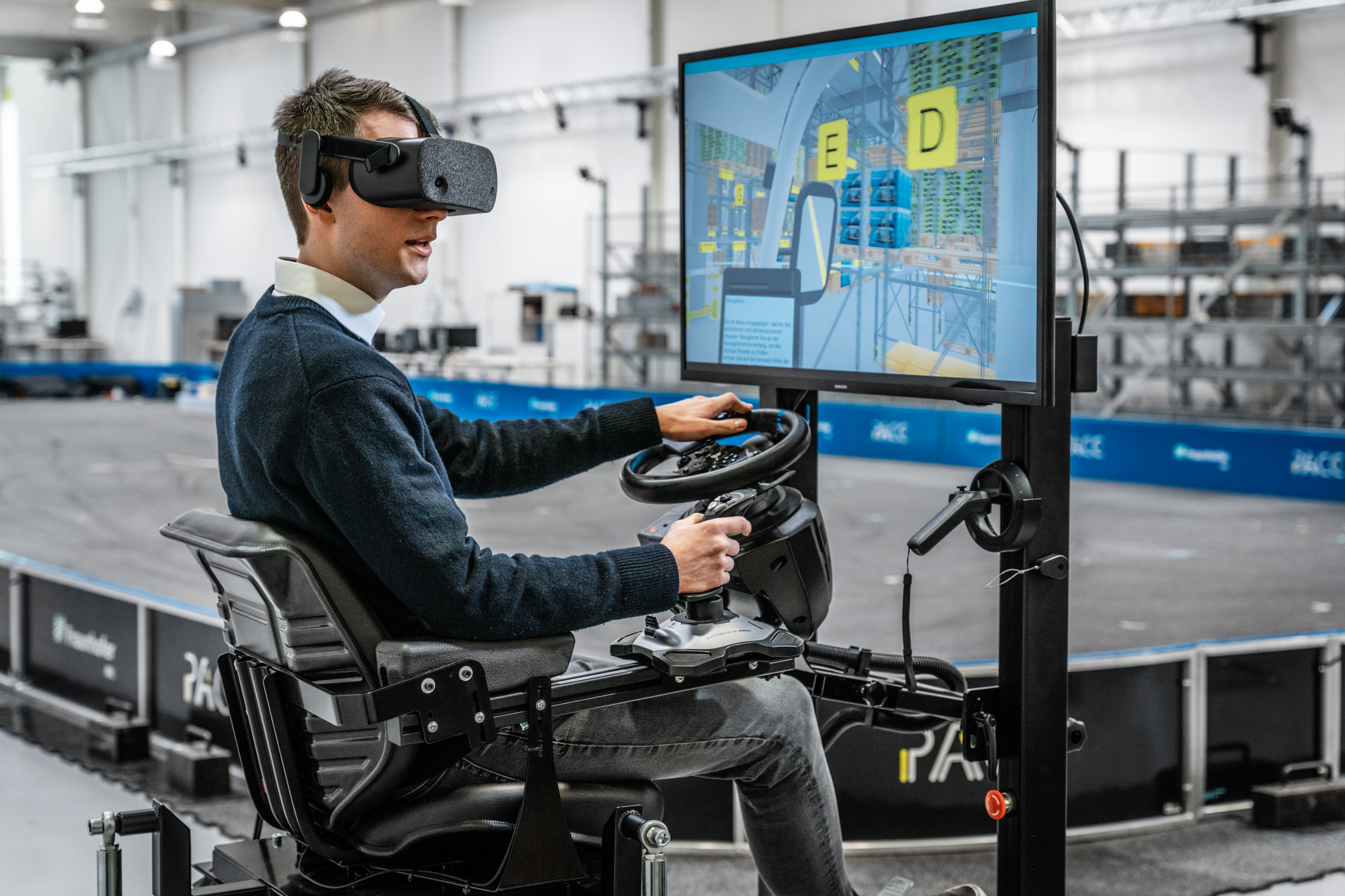 Ein Mann sitzt an einem Bildschirm und trägt eine VR Brille, während er einen Gabelstapler in einer Simulation fährt.