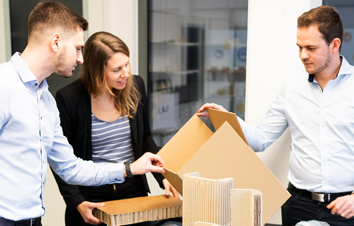 The picture shows three people looking at an environmentally sustainable packaging. As part of the SustainPack project by Fraunhofer IML, packaging systems were assessed ecologically.
