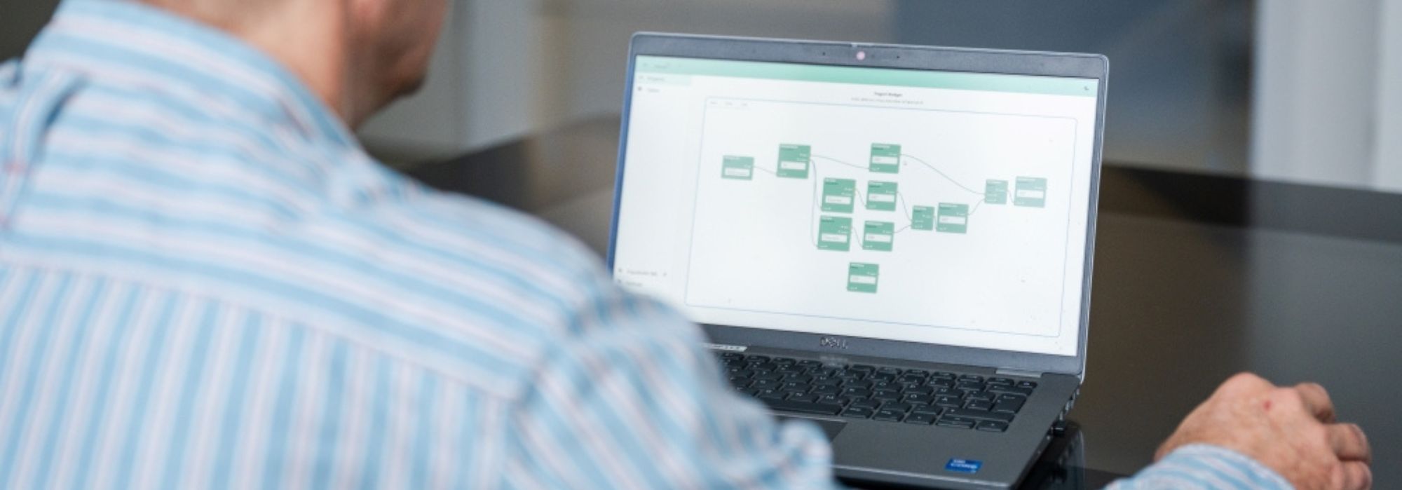 The image shows a man sitting at a computer, photographed from behind, with a graphic visible on the screen.