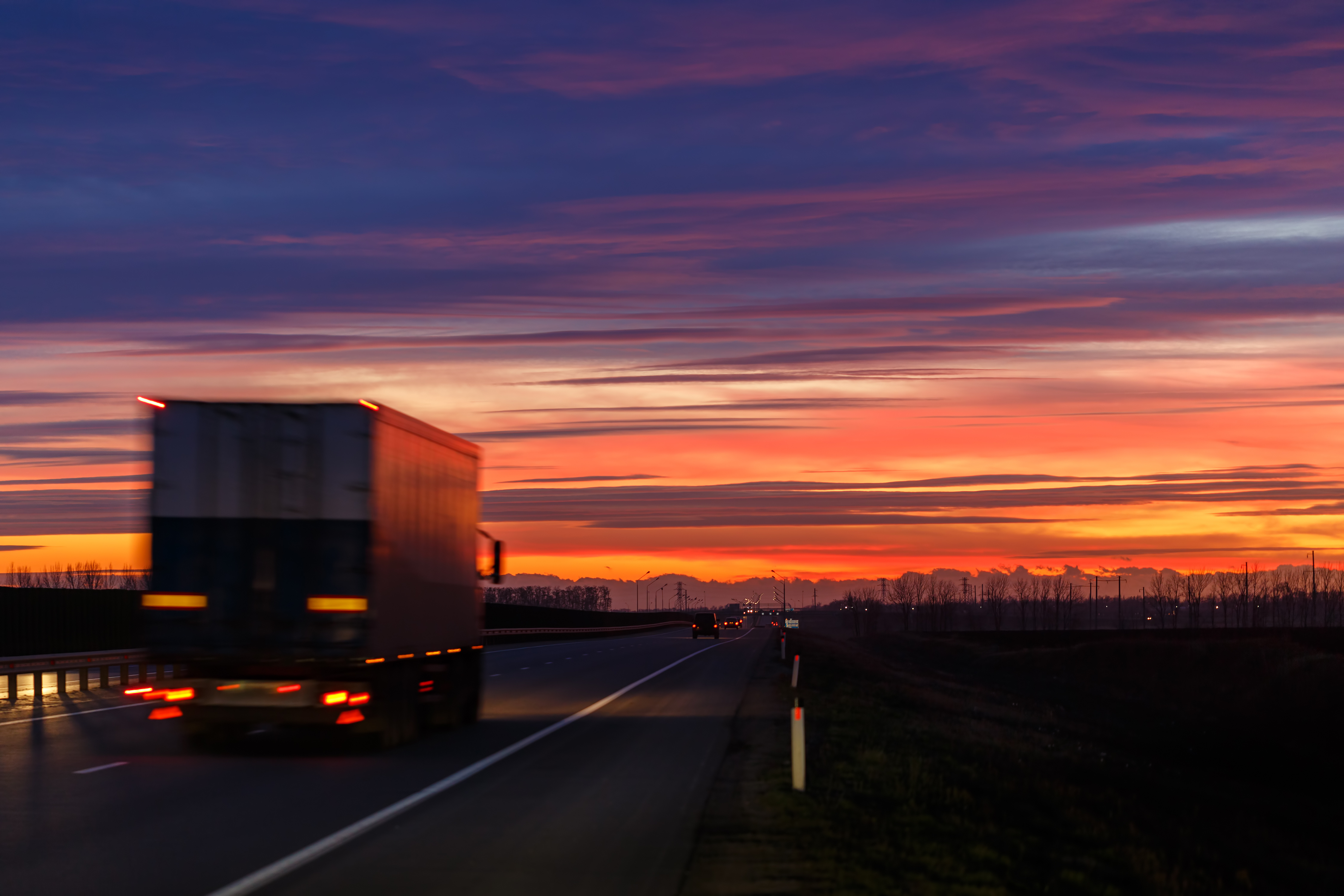Ein LKW fährt während eines farbenfrohen Sonnenunterganges über eine Straße.