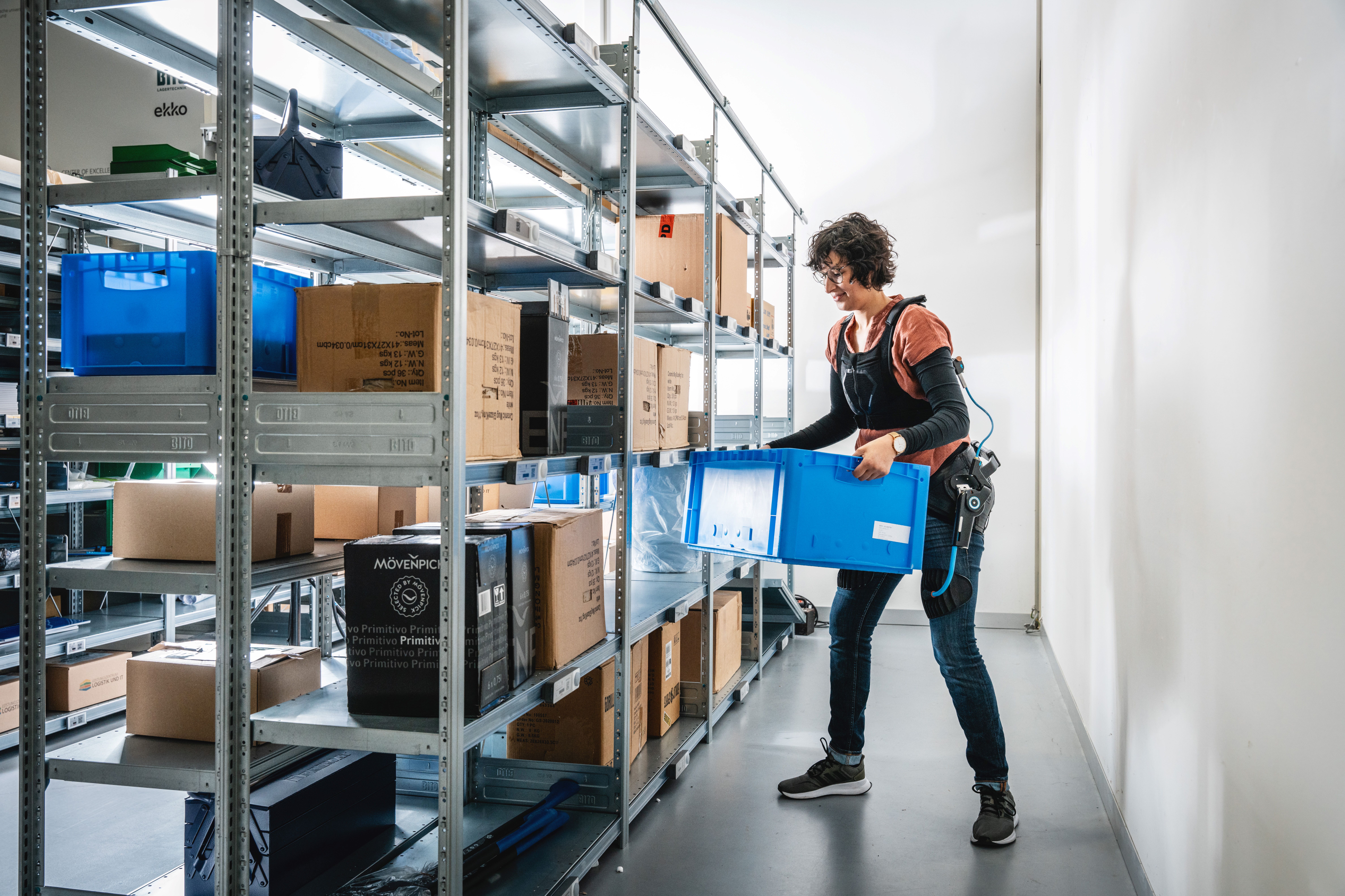 A woman using an exoskeleton lifts a box